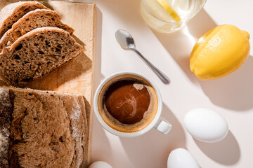 top view of bread, eggs, lemon water and cup of coffee for breakfast on grey table