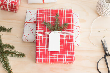 Red and white christmas gifts surrounded with pine cones, leaves and twine on a wooden table.