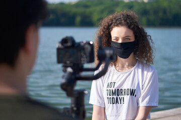 A young woman in medical mask filming by a man