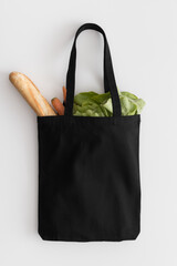 Black tote bag mockup with groceries on a white table.