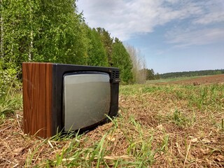 an old tv set lies in a field near a forest against a blue sky