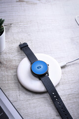 Smart watch on wireless charging with on-screen charging indicator. At the desktop, near at the laptop. Top view.