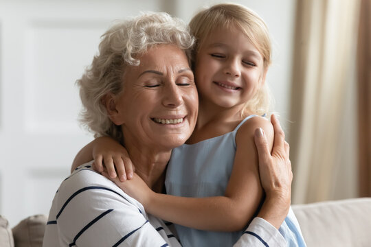Close up view loving grandmother cuddle snuggle to small granddaughter people closed eyes enjoy tender moment express cherish and sincere affection, sit on sofa in living room, love protection concept