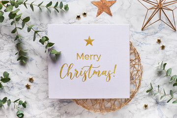 Obraz na płótnie Canvas Christmas frame with fresh eucalyptus twigs and golden geometric decorations - hexagons, trinkets and wire shapes. Flat lay, top view on white marble background with text Merry Christmas in gold.
