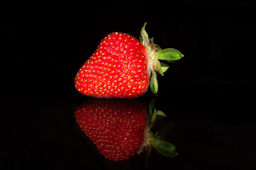 One strawberry isolated on a black background with mirror reflection.
