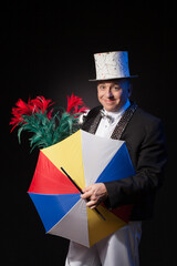 Magic man with flowers  and umbrella  in black suit and white silk hat on isolated black background 