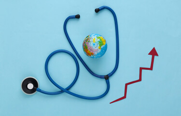 Global medicine concept. Stethoscope with globe, growth arrow on blue background. Top view