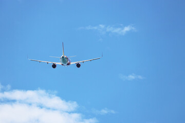 Airplane flying in the blue sky on background of white clouds, rear view. Twin-engine commercial plane during the turn, turbulence and travel concept