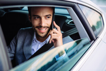 Businessman talking on a phone and looking through the window from the car