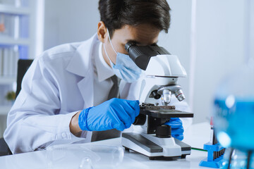 Young Asian handsome man scientist adjust focus and use Microscope to looking biochemical cell in laboratory. Doctor and scientist work in laboratory pandemic of corona virus, COVID19 concept