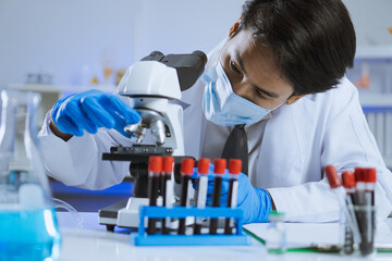 Young Asian handsome man scientist adjust focus and use Microscope to looking biochemical cell in laboratory. Doctor and scientist work in laboratory pandemic of corona virus, COVID19 concept