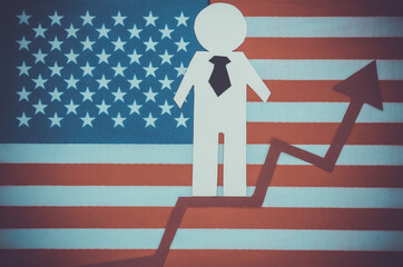 Paper business man with growth arrow on background of USA flag. Symbol of financial and social success, stairway to progress. Career ladder.