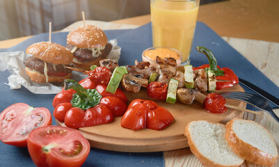 spring vegetables - bell peppers, cucumbers, onions, lettuce, tomato with grilled kebabs and orange juiceon a blue tablecloth