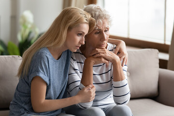 Seated on couch in living room grown up adult daughter soothes elderly mother, shares her mental...