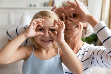 Close up funky old grandma small granddaughter with funny faces making binoculars with fingers like...