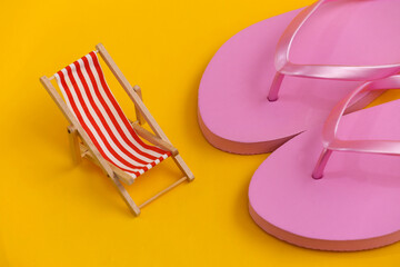 Flip flops and mini beach deck chair on yellow background. Symbol of beach holidays, resort.  Relax, Summer minimal concept