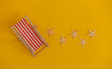 Mini beach deck chair and starfish on yellow background. Symbol of beach holidays, resort.  Relax,...