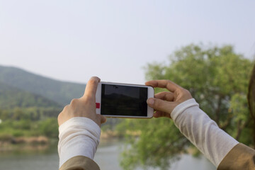 Using smart phone, woman photographs spring landscape with green tree.