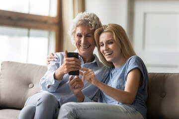 Elderly mom and grown up daughter watching funny video laughing having fun in internet, teenage granddaughter aged grandma having conversation by videocall, taking self-portrait on smart phone concept