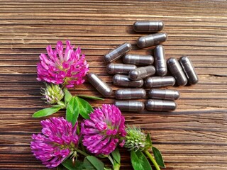 Bunch of red clover flowers (Trifolium pratense) & pills close up. Spring red or pink clover flowers bouquet, capsules on brown wooden table, top view. Purple red wild clover field flowers supplement