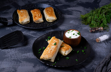 Pancakes with filling are served on the black plate with sour cream