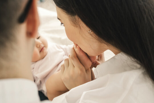 Mom And Dad, Mother Hold And Kiss Baby Legs. Taking Care Of A Newborn.