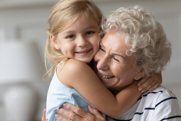 Close up image portrait happy small cutie granddaughter hugging with caring old grandmother, multi generational family relatives people snuggle to each other feeling love and strong connection concept