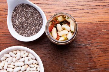 Nutrition concept - Healthy meal of white beans, chia and vegetables in glass jar over wooden background. Glass cup on wood table, benefits for diet, weight control and diabetes
