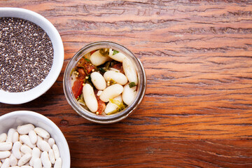 Nutrition concept - Healthy meal of white beans, chia and vegetables in glass jar over wooden background. Glass cup on wood table, benefits for diet, weight control and diabetes