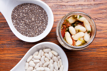 Nutrition concept - Healthy meal of white beans, chia and vegetables in glass jar over wooden background. Glass cup on wood table, benefits for diet, weight control and diabetes