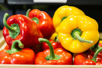 Close-up of red and yellow pepper lying on shelf in grocery. Colorful vegetables for sale in retail shop. Vegan food, healthy eating, bell pepper.