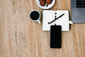 Flat lay of the workplace. Freelance work laptop smartphone and note pad. Morning coffee with cookies. Copy space on wooden background and notepad.