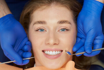 A close photo of a pretty woman who is being examined by a dentist with dental tools in a dental...