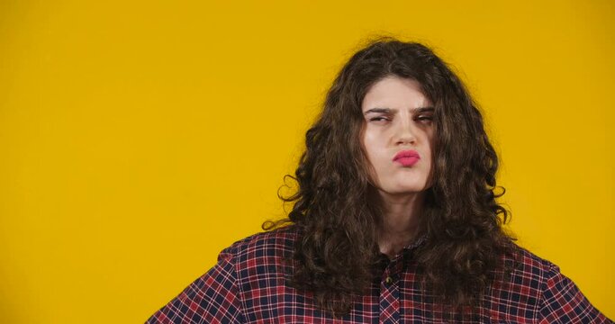 Close-up attractive plus-size model posing. A curly-haired brunette on bright yellow studio background demonstrating different emotions. Pensive girl is thinking hard
