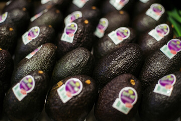 Avocados with blurred labels lying in supermarket. Bunch of fresh organic nutritional fruits in retail grocery. Vitamins, healthy eating, dieting.
