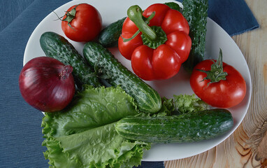 spring vegetables - bell peppers, cucumbers, onions, lettuce, tomato on a white plate
