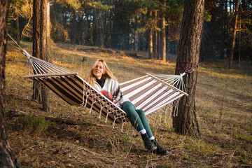 Young attractive woman laying in the hammock in sunny forest, resting after active hike - photo with selective focus