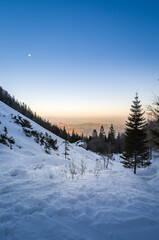 Snowy landscape in mountains. Golden hour sunset with visible moon in the sky. Winter season in Alps, Slovenia. Late evening hiking