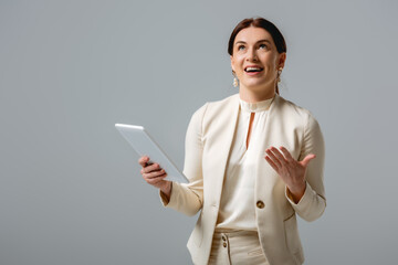 Positive businesswoman looking up during video call on digital tablet isolated on grey