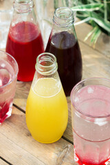Strawberry, cherry and rhubarb syrups and glasses with water on a wooden table in the garden.