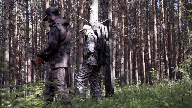 Two hunter men in camouflage clothes with guns walking through forest during hunting season. Man hunter outdoor in forest hunting. Male Tourists