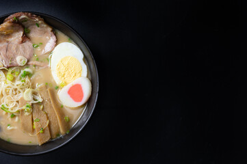 Delicious tonkotsu ramen, Japanese noodle in pork Bone based soup topped with sliced chashu pork, boiled egg, pickled bamboo shoot and spring onions. top view on black background with copy space. 