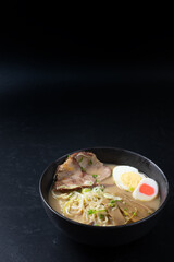 Delicious tonkotsu ramen, Japanese noodle in pork Bone based soup topped with sliced chashu pork, boiled egg, pickled bamboo shoot and spring onions. on black background with copy space.