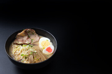 Delicious tonkotsu ramen, Japanese noodle in pork Bone based soup topped with sliced chashu pork, boiled egg, pickled bamboo shoot and spring onions. on black background with copy space.