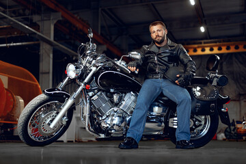 Fototapeta na wymiar Bearded motorcyclist in black leather clothing with his motorbike