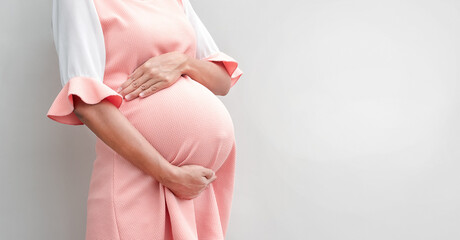 Pregnant woman in dress holds hands on belly on a white background , copy space