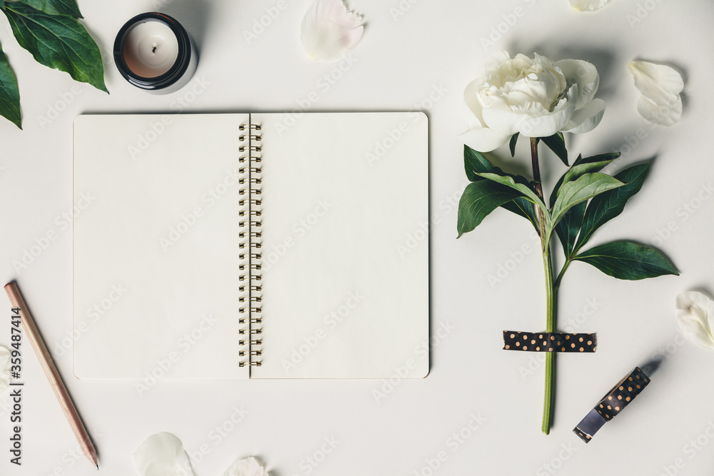 Wall mural flat-lay of beautiful peony flower taped on white background and open notebook