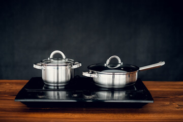 induction cooker with pans standing on wooden countertop on dark background