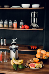 juicer with orange, grapefruit, kiwi, banana and avocado standing on wooden countertop on modern kitchen