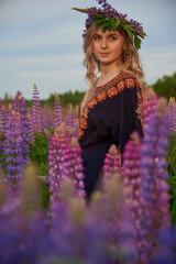 Fototapeta na wymiar A charming blonde girl with long wavy hair poses in a field with bright lupines.